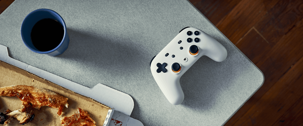 A Stadia controller next to a pizza and a cup