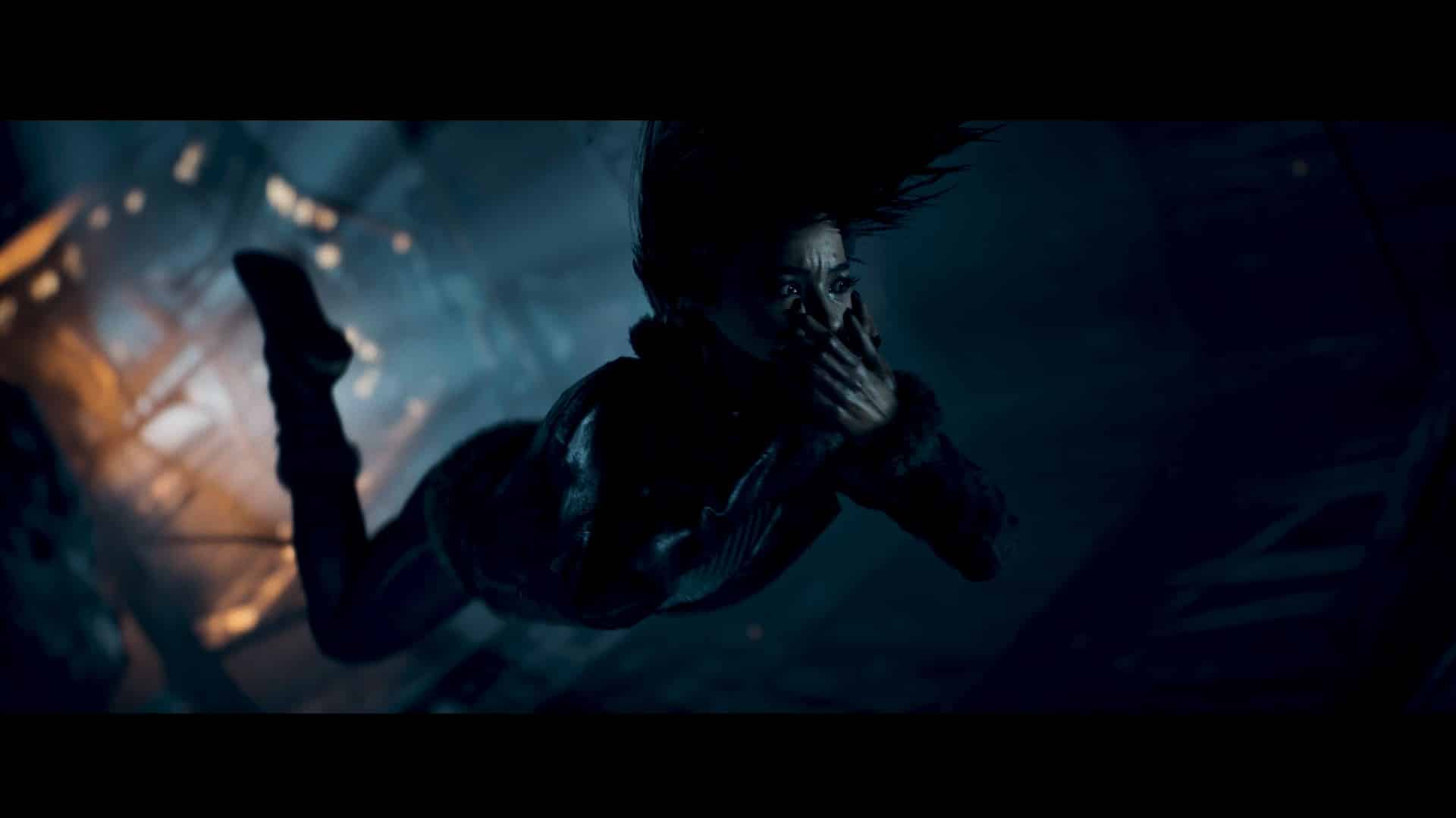 In a dark, dramatic scene from Until Dawn (2024), Emily is suspended mid-air, covering their mouth with a look of surprise or fear.