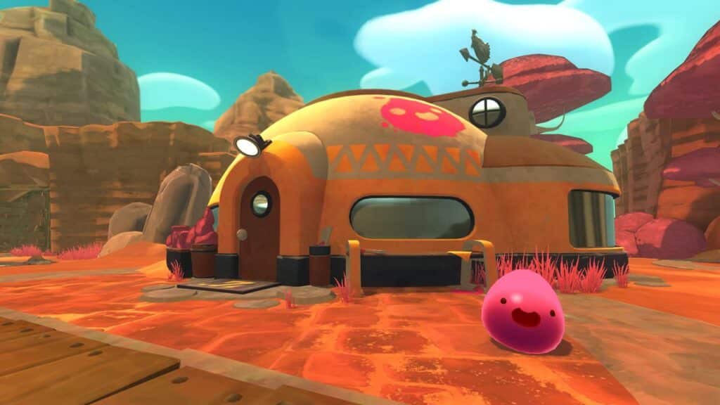 In a cartoonish desert scene, a round, orange building stands prominently while a smiling pink blob reminiscent of Slime Rancher joyfully sits in the foreground.