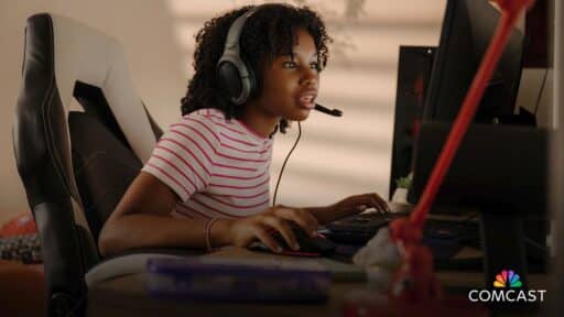 Teen girl intensely gaming at a computer with a headset, sitting in a chair, focused on the screen. With Comcast ultra-low lag Internet, her gameplay is seamless and uninterrupted, ensuring every second counts in her virtual world.