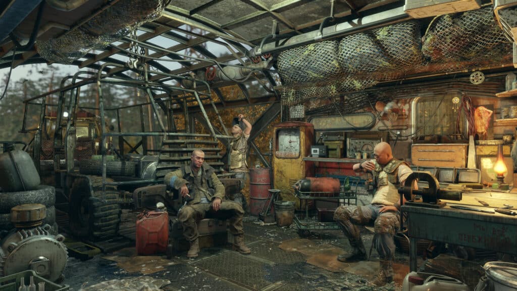 Three people sit and stand in a cluttered, rustic workshop reminiscent of a Metro Exodus setting, filled with tools, equipment, and a rugged vehicle.