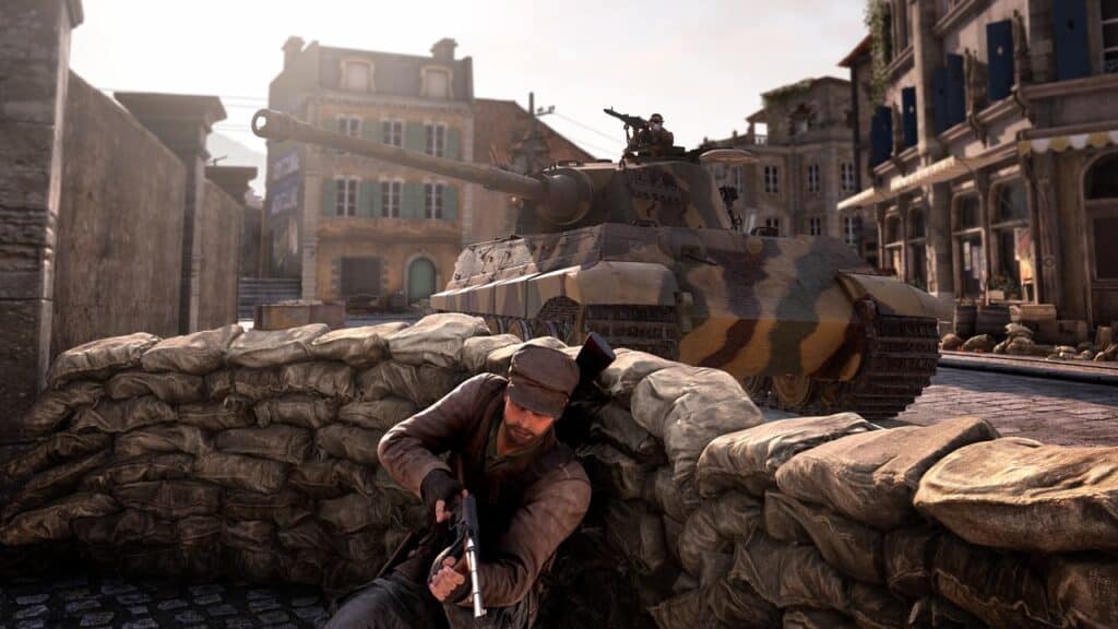 Amidst the chaos of a war-torn town, a soldier crouches with a gun behind sandbags. Channeling the spirit of Sniper Elite: Resistance, a tank rumbles nearby as the gunner scans the street for threats.