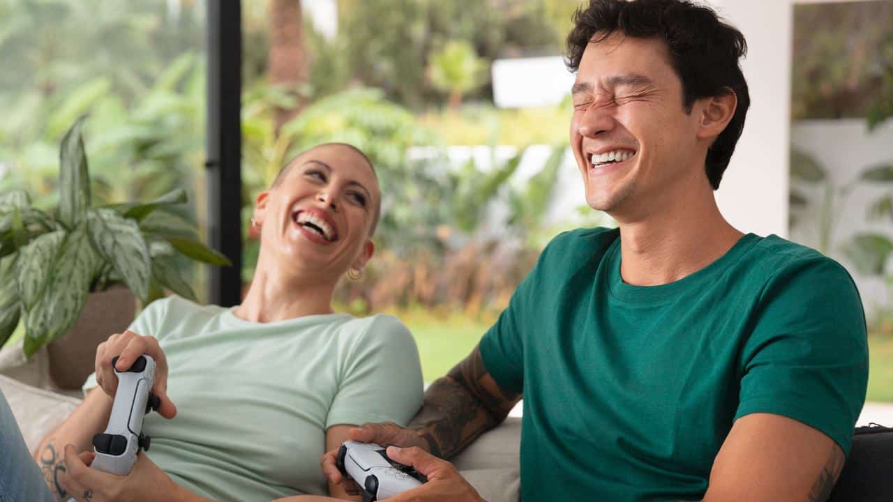 A smiling couple enjoys exploring video games to play with your girlfriend or boyfriend as they relax on the couch, holding controllers.