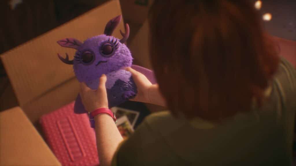 A person cradles a cute, plush purple creature with antler-like ears and big eyes, reminiscent of characters from Lost Records: Bloom & Rage, standing by an open cardboard box.