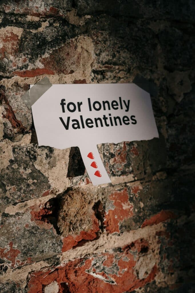 A paper sign with "for lonely Valentines" and heart graphics taped to a brick wall invites passersby to join Valentine's Day games for singles.