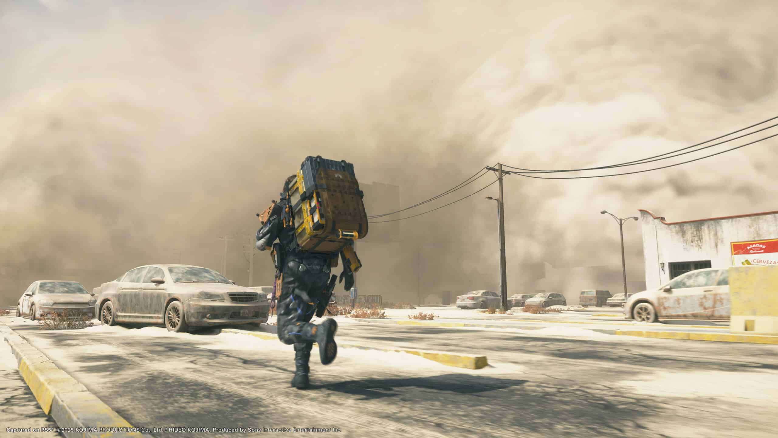 A lone traveler with a large backpack races down a snow-covered road, a dust storm on the horizon and parked cars all around, reminiscent of scenes from Death Stranding 2.