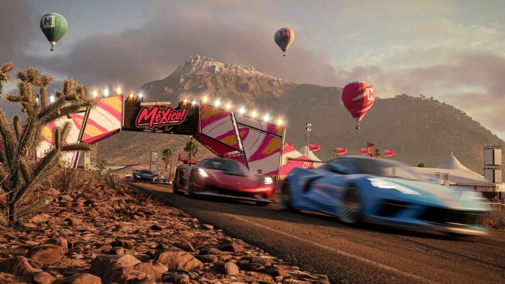 Sports cars race on a desert road with hot air balloons and mountains in the background at a festival in Mexico, capturing the thrilling spirit of Forza Horizon 5 PS5.