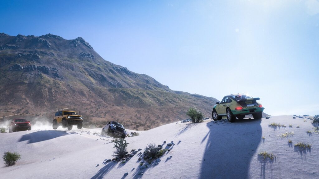 Four off-road vehicles drive over sandy dunes with a mountain and clear blue sky in the background, capturing the exhilarating adventure found in Forza Horizon 5 PS5.