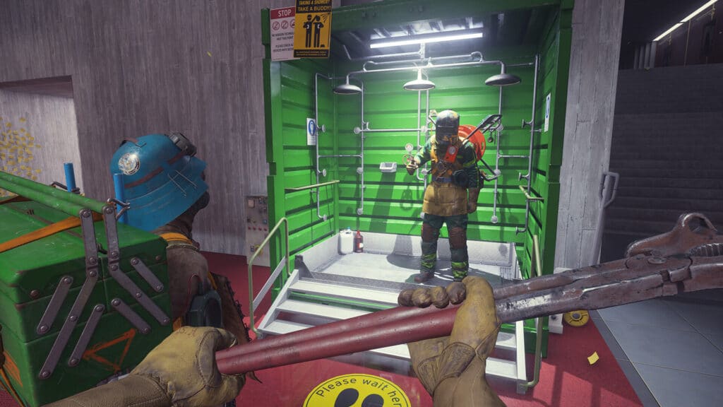 First-person view of a character holding a large wrench, facing another person in protective gear inside a green booth during the FBC: Firebreak livestream.