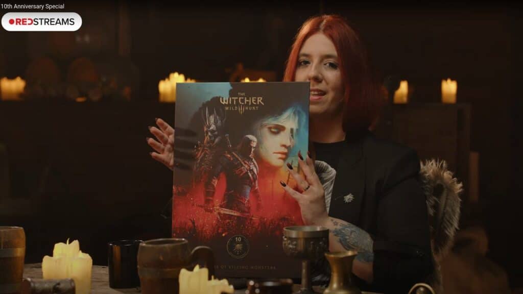 A person with red hair holds up a The Witcher 3 anniversary poster in a candlelit room, celebrating a decade of Wild Hunt adventures.