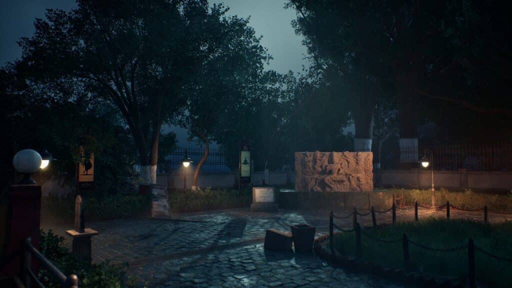 A quiet, stone-paved park at night, lit by lampposts, with trees and a large stone sculpture symbolizing Mukti.