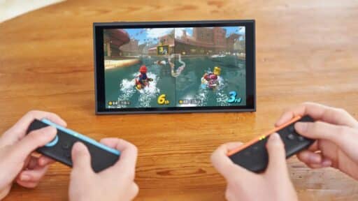 Two people playing Mario Kart World on a Nintendo Switch 2 with Joy-Con 2 controllers and Nintendo Switch 2 accessories on a wooden table.