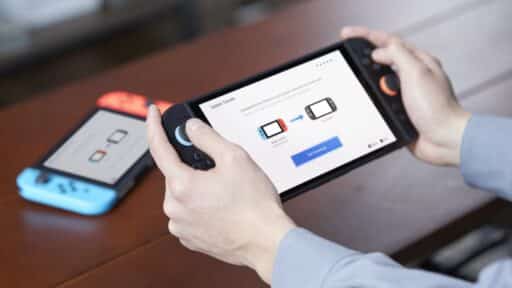 Person holding a Nintendo Switch 2 near a Nintendo Switch on a table, with a Nintendo Switch to Nintendo Switch 2 data transfer screen displayed.