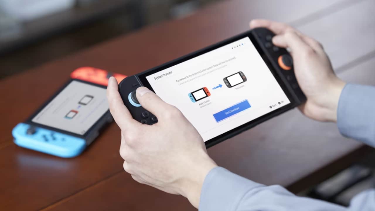 Person holding a Nintendo Switch 2 near a Nintendo Switch on a table, with a Nintendo Switch to Nintendo Switch 2 data transfer screen displayed.