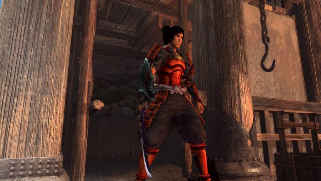 A samurai in red armor stands in a wooden building with a large metal hook hanging nearby, evoking the atmosphere of Onimusha 2: Samurai’s Destiny Remaster.