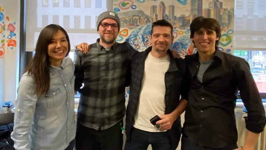 Four people smiling and standing together indoors with a colorful mural and cityscape in the background, including Alex Hutchinson of Google Stadia.