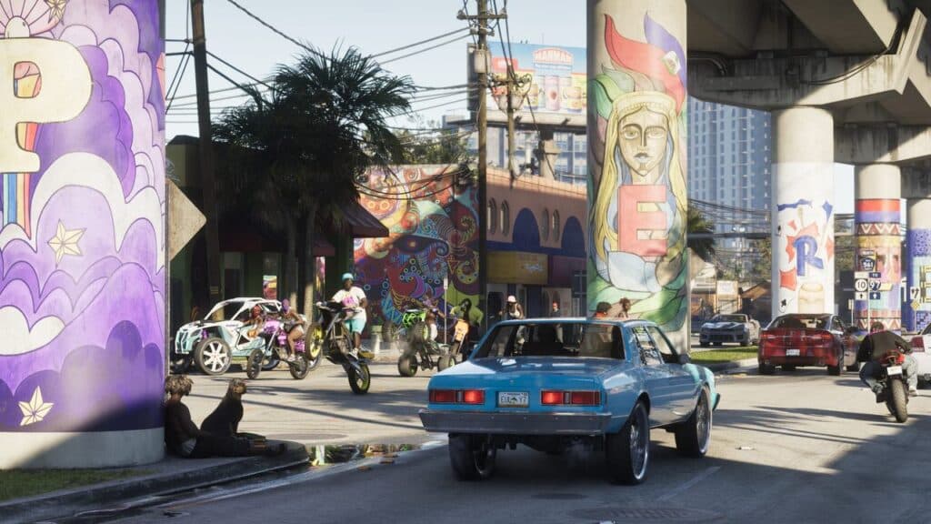A blue car drives under a bridge with colorful murals, as people ride motorcycles nearby—capturing the lively vibe seen in the second GTA VI trailer.