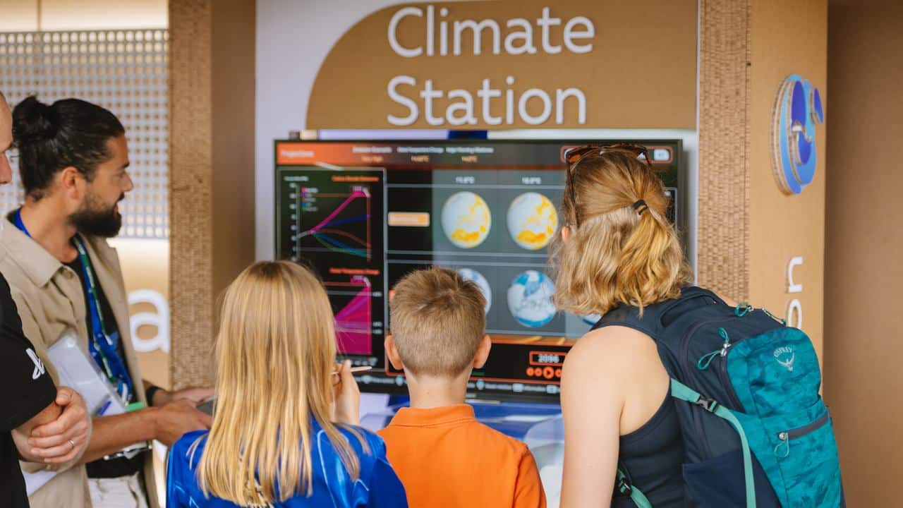 Three children and two adults look at climate data on a screen at the Climate Station PlayStation exhibit.