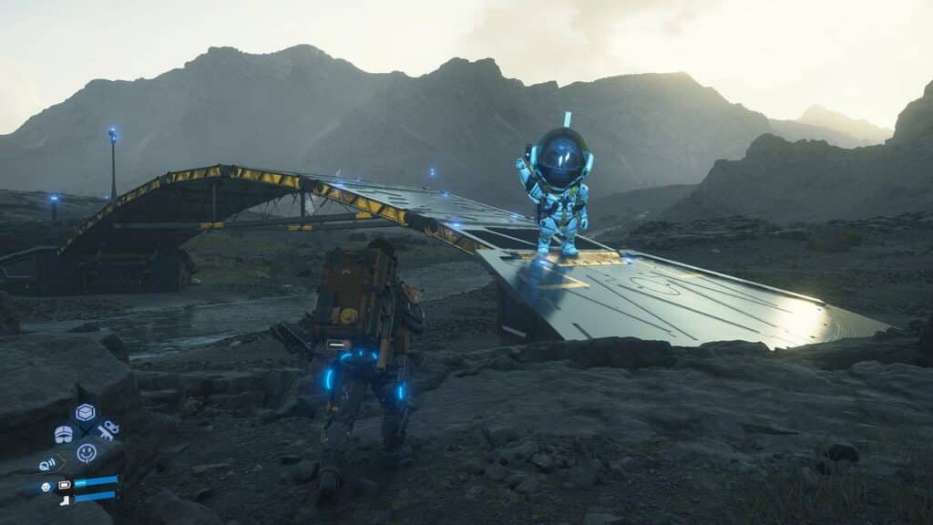 A character in a spacesuit stands on a futuristic bridge in a rocky, mountainous landscape at dusk, evoking the mysterious world of Death Stranding 2: On The Beach.
