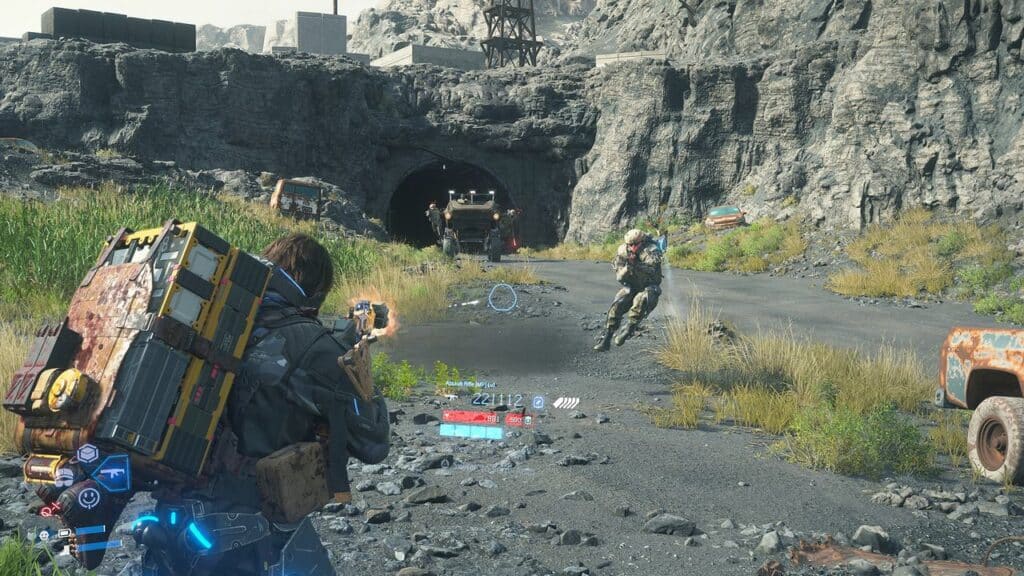A character with a large backpack aims a weapon at a biker near a tunnel in a rocky, post-apocalyptic landscape reminiscent of Death Stranding 2: On The Beach.
