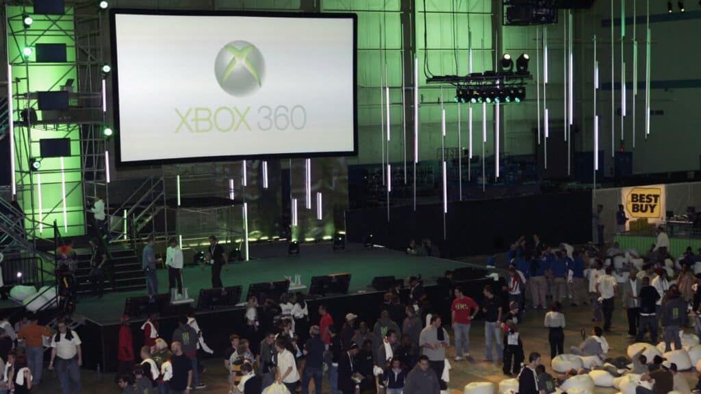A crowd gathers at an event with an Xbox 360 logo on a large screen, green lighting highlighting the scene where Laura Fryer Xbox is celebrated.