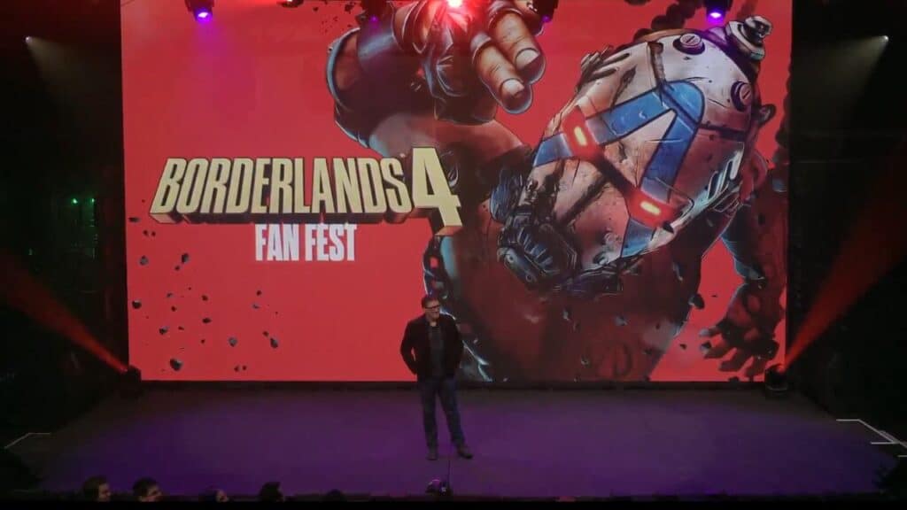 A man stands on stage in front of a large Borderlands 4 Fan Fest screen with a masked character, ready to unveil the exciting Borderlands 4 Story Trailer.