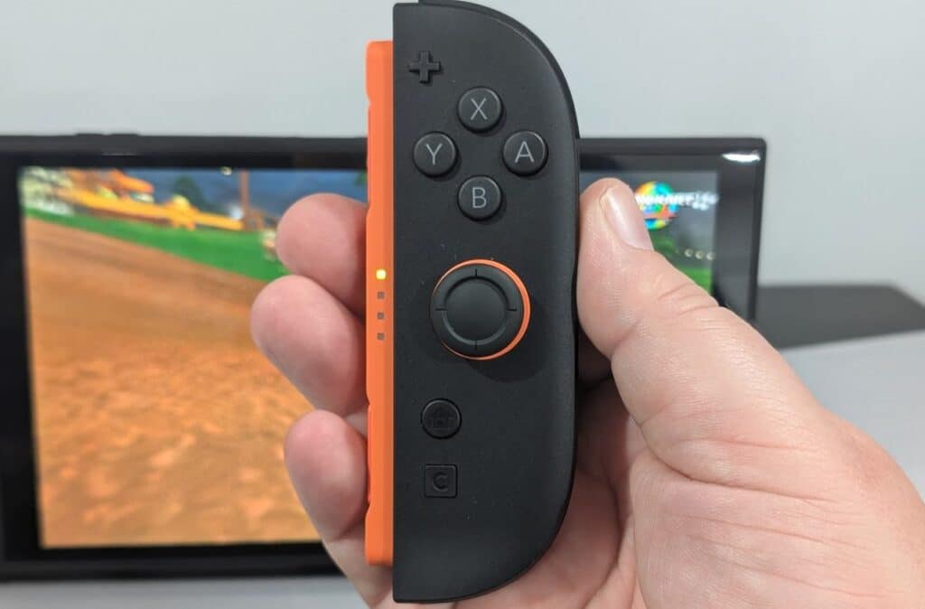 A hand holding a Nintendo Switch 2 Joy-Con 2 controller in front of the Nintendo Switch 2.