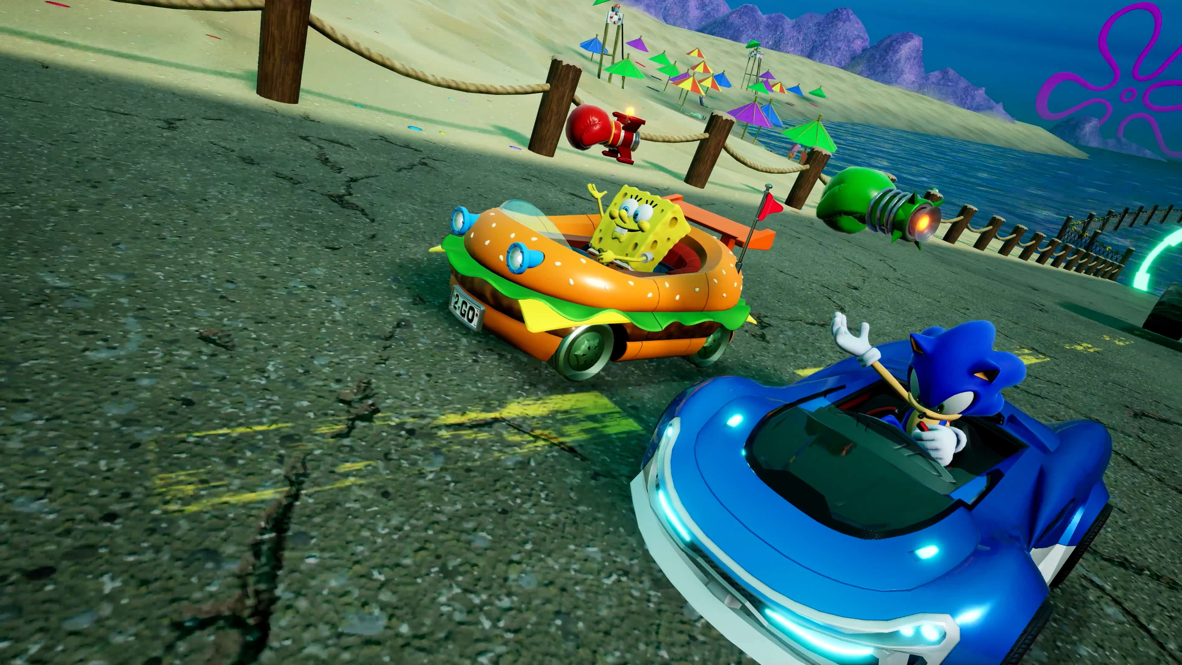 SpongeBob and Sonic race colorful cars on a beachside track with ocean and umbrellas in the background.