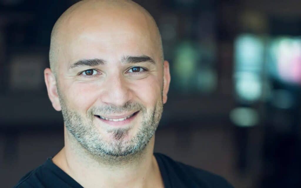 IO Interactive CEO Hakan Abrak smiles at the camera during an IO Interactive interview, wearing a black shirt with a blurred background.