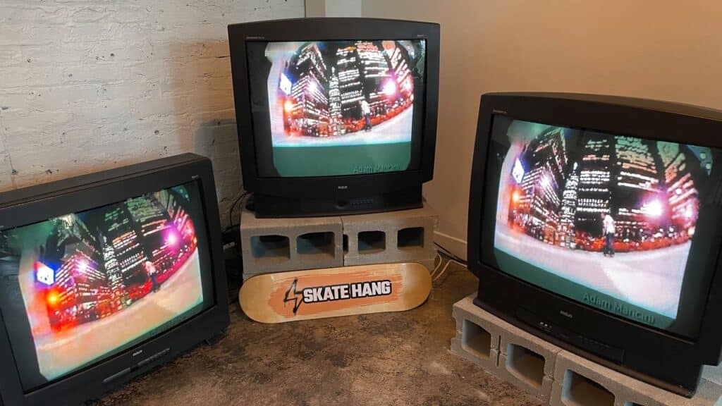Three old TVs on cinder blocks display a fisheye city scene, with a skateboard labeled "Skate Hang" in front—evoking the vibe of Tony Hawk’s Pro Skater 3 sessions.
