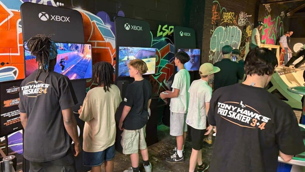 A group of kids enjoy a Tony Hawk’s Pro Skater 3 + 4 Skate Hang on Xbox consoles in a graffiti-decorated room.