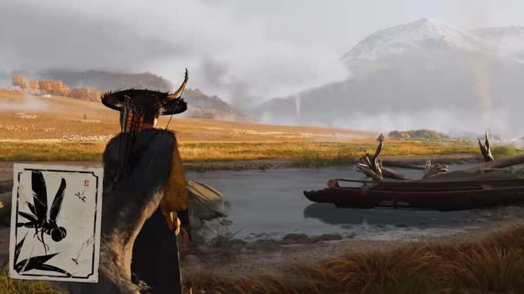 A person in traditional attire stands by a calm river with boats, mountains, and fields in the background.