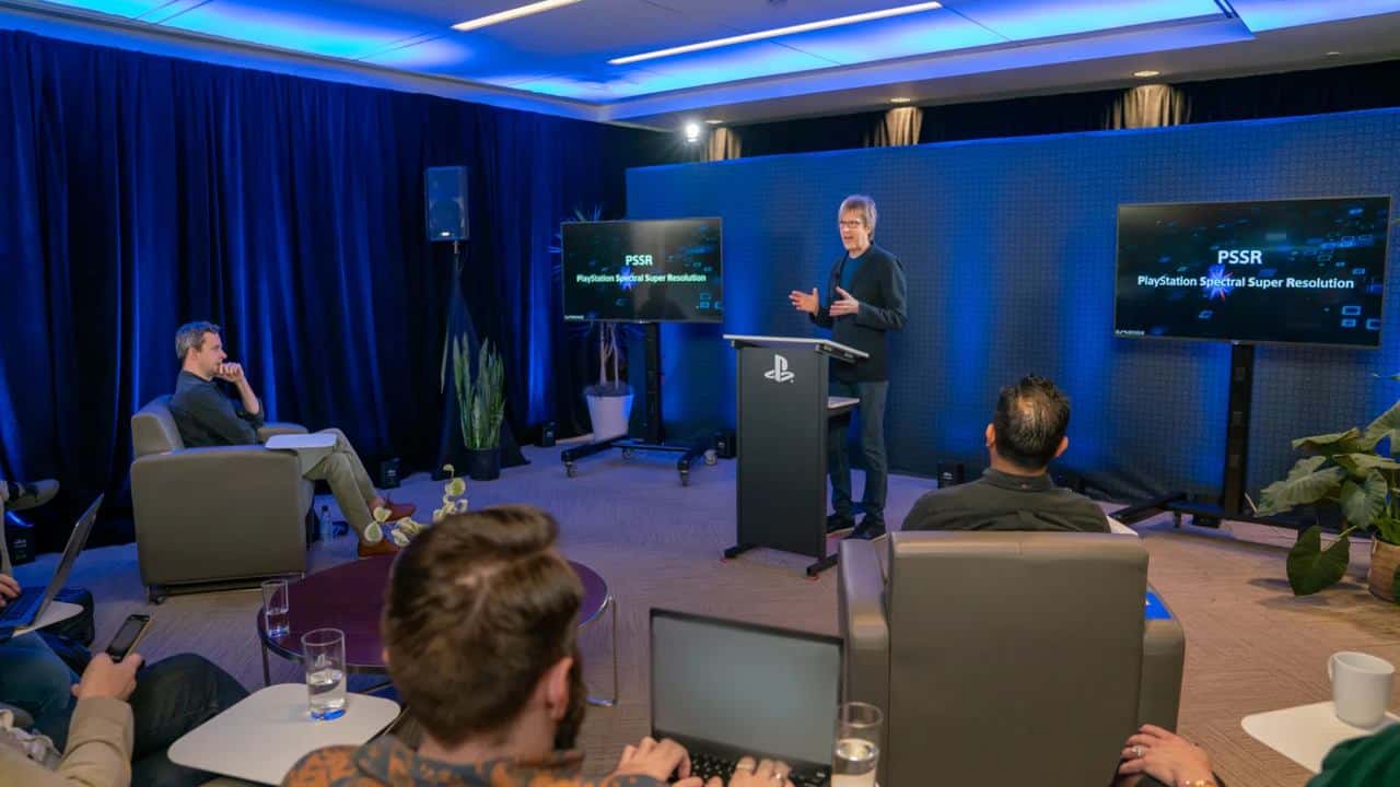 A presenter speaks at a PlayStation event with seated attendees and screens displaying "PSSR," highlighting the PS5 Pro PSSR upgrade.