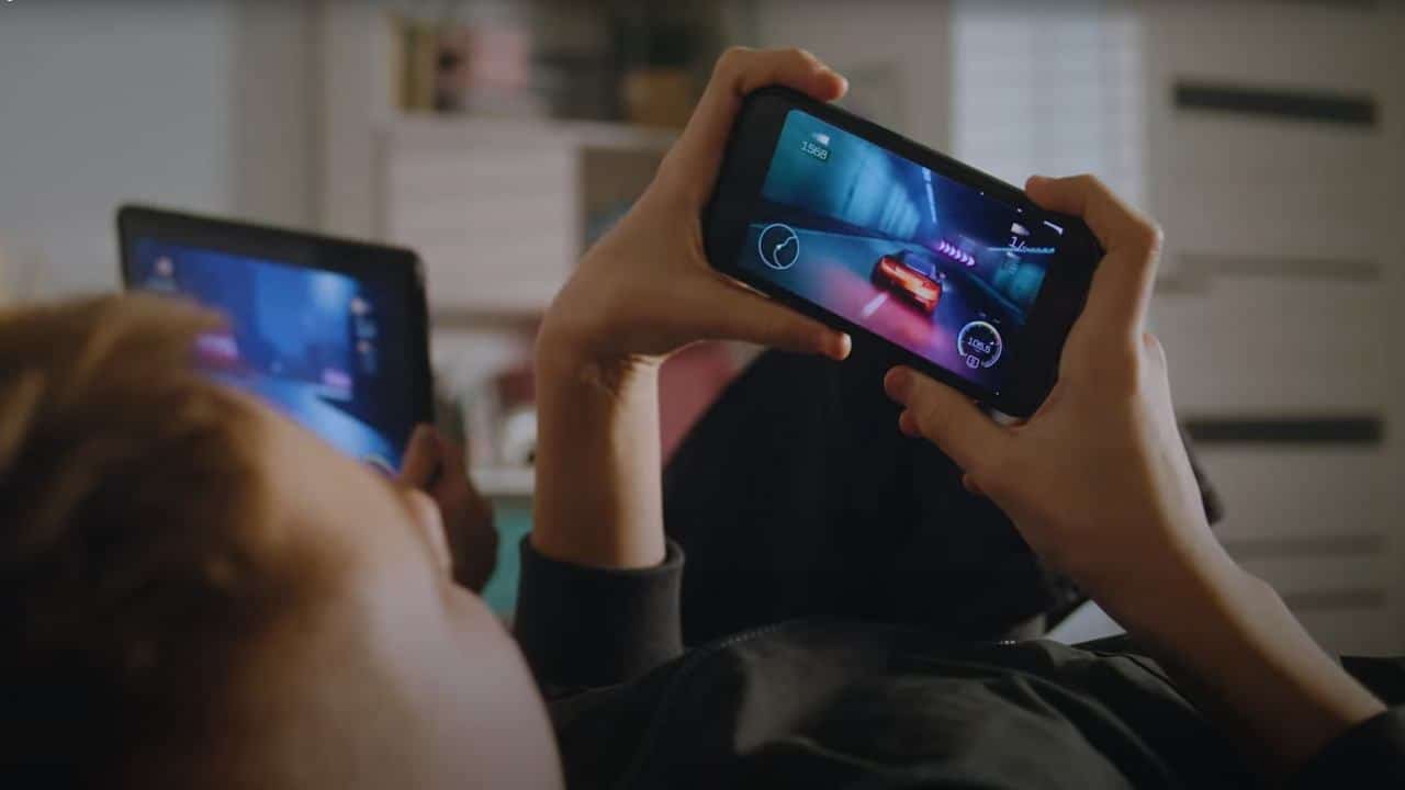 Relaxing while playing a racing game on a smartphone, with T-Mobile L4S ensuring ultra-smooth gameplay and another screen visible in the background.