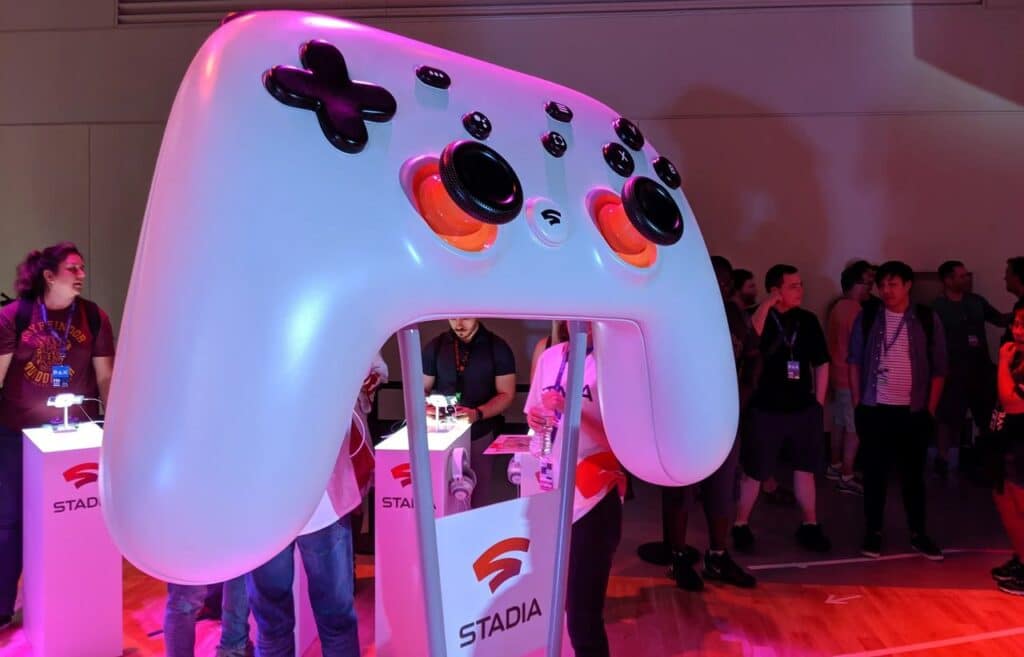 A giant Stadia controller prop on display at an event, surrounded by people, Stadia booths, and guided tours led by the former Google Stadia Community Manager.