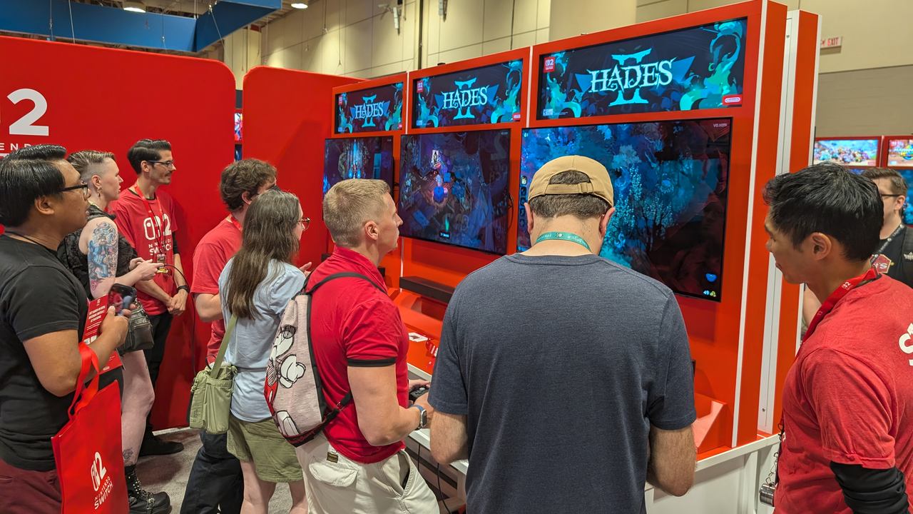 People at Fan Expo Canada 2025 share their Hades II hands-on impressions as they play on large screens at a Nintendo booth.