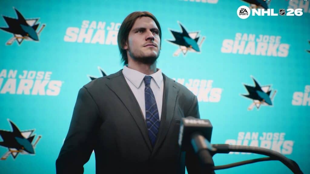 A man in a suit stands at a podium with San Jose Sharks and EA Sports NHL 26 logos in the background.