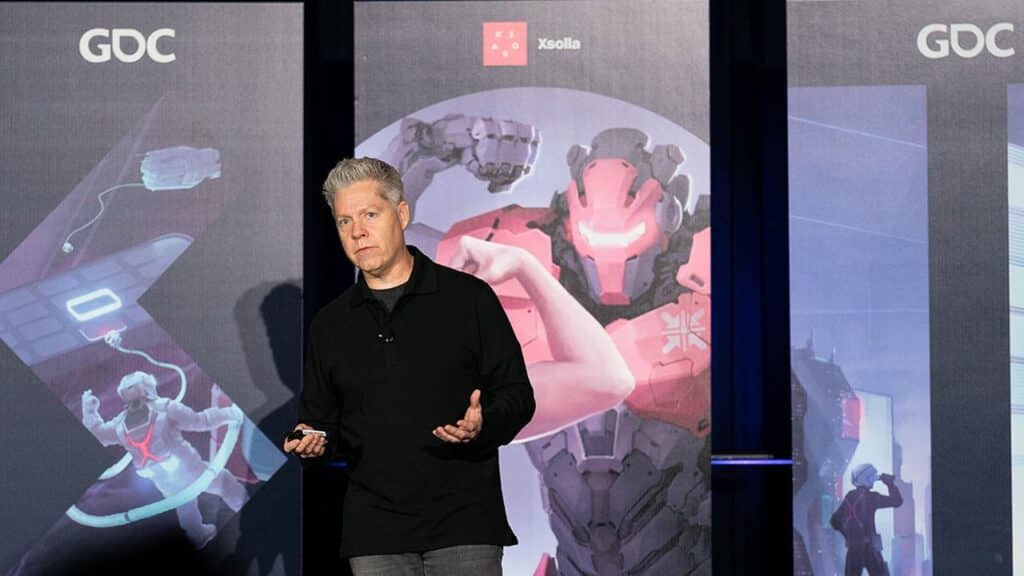 Chris Hewish speaks on stage at GDC, standing in front of a large gaming-themed backdrop while discussing Xsolla cloud gaming trials.