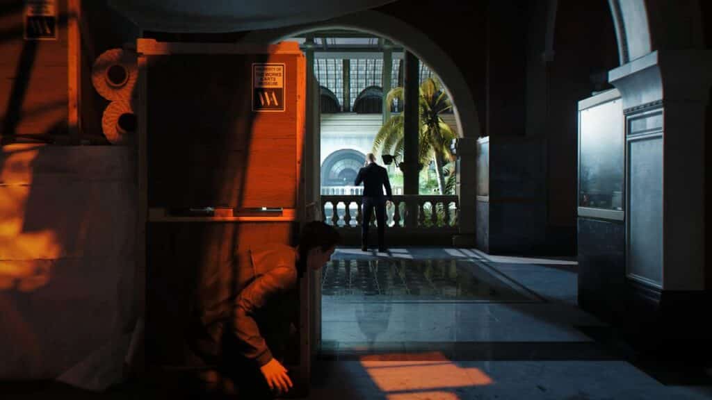 007 James Bond crouches behind crates inside a grand building, watching another by a balcony—capturing the suspenseful style of 007 First Light State of Play.