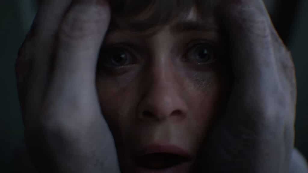 A frightened person’s face is held tightly by two pale, gray hands, eyes wide with fear—capturing the haunting intensity OD Knock an upcoming video game from Kojima Productions.