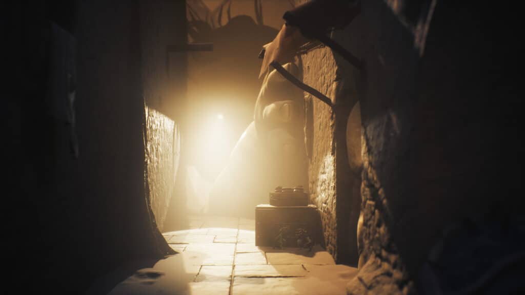 A dim, narrow stone hallway, from Little Nightmares III, with light shining at the far end and eerie shadows flickering on the walls.