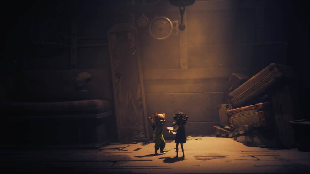 Low and Alone stand in a dim, dusty room filled with old furniture and scattered debris, lit by a soft light—a scene from, Little Nightmares III.