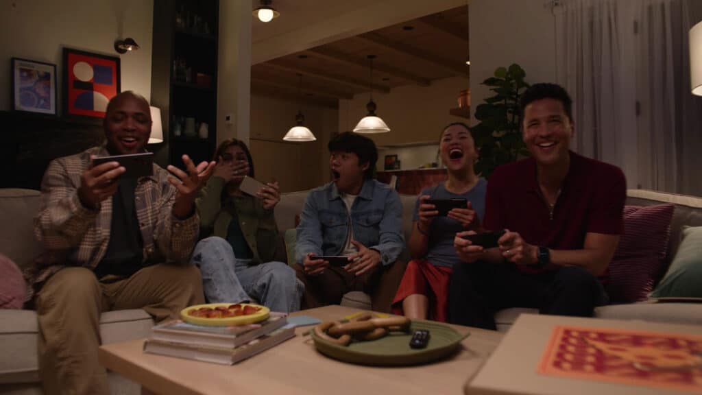 Five friends sit on a couch, laughing and playing games on their phones with the GameNight and Social Play in the All New Amazon Luna in a cozy living room.