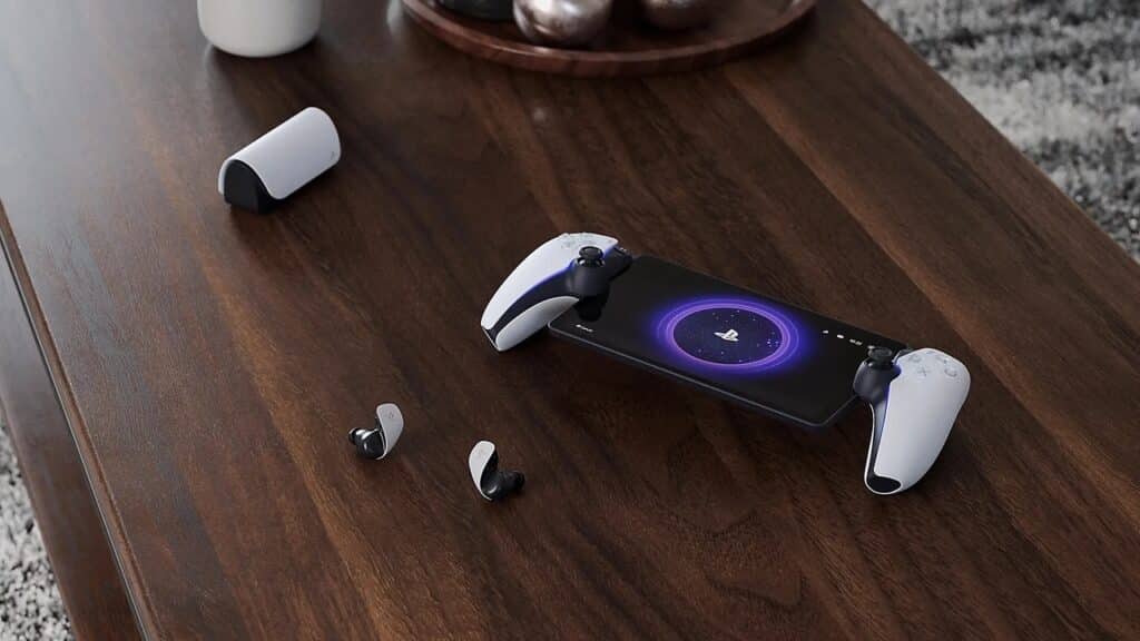 PlayStation Portal on a desk with wireless earbuds, and a charging case on a wooden table—showcasing some of the best PlayStation Portal accessories for your gaming setup.
