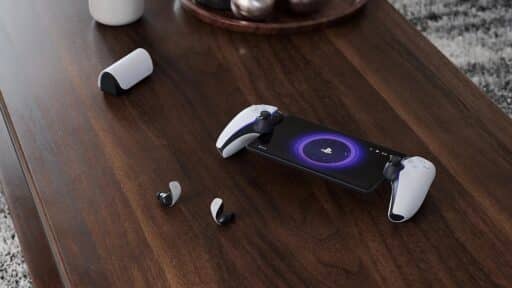PlayStation Portal on a desk with wireless earbuds, and a charging case on a wooden table—showcasing some of the best PlayStation Portal accessories for your gaming setup.
