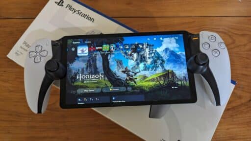 PlayStation Portal handheld device displaying a game menu, highlighting cloud gaming on PlayStation Portal, resting on a PlayStation box on a wooden surface.