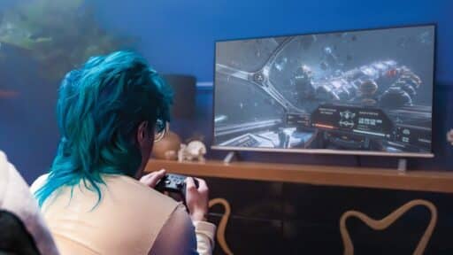 Person with teal hair playing a space-themed video game via Amazon Luna cloud gaming on a large TV in a cozy room.