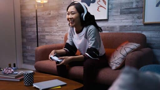 Woman smiling while playing a video game on a couch, wearing headphones and holding a controller—enjoying seamless gaming powered by PlayStation Network AWS.