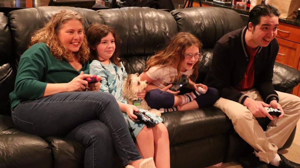 A family of four and a small dog sit on a couch, smiling as they enjoy video games together on their Smart TV, embracing the future of cloud gaming.