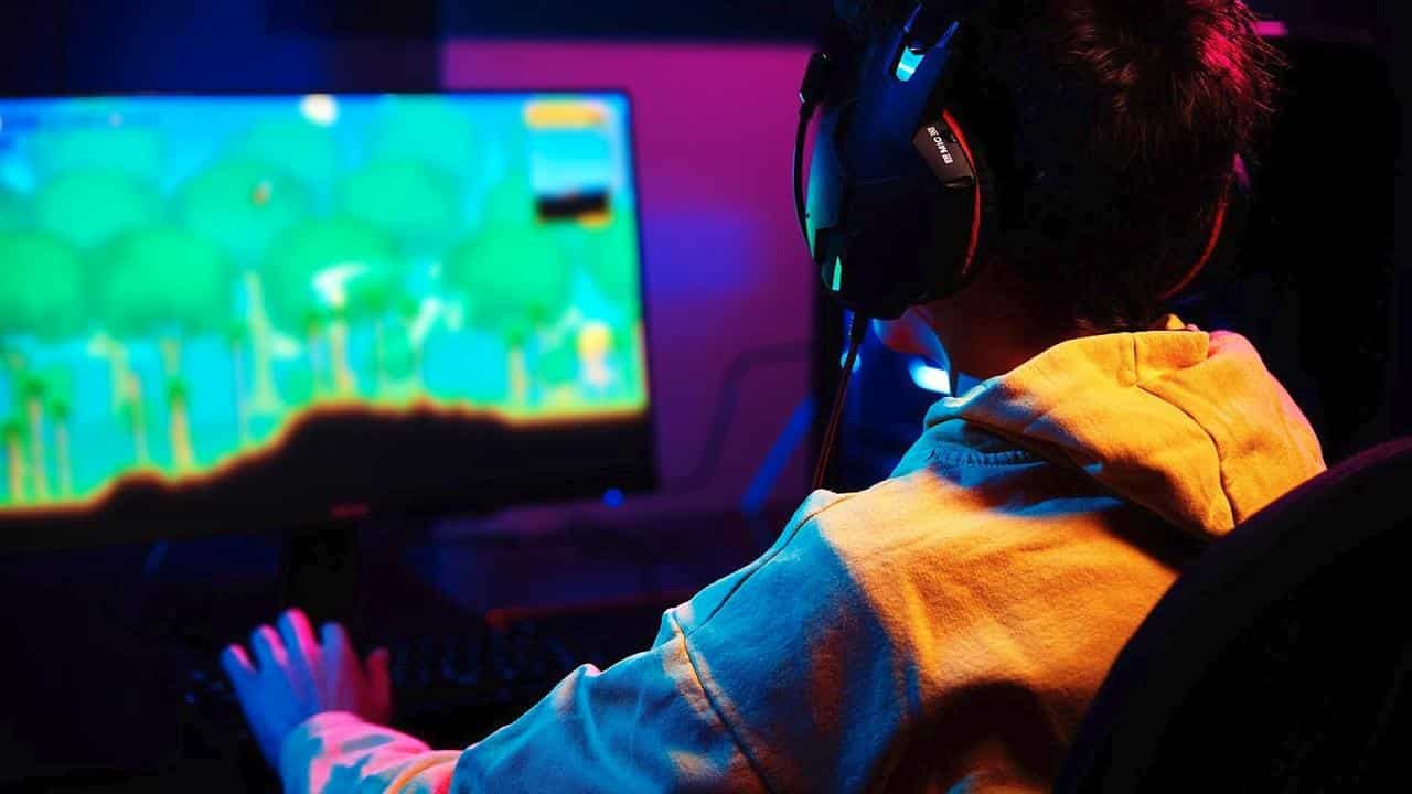 Person in a yellow hoodie playing a colorful video game on a computer with a headset on, highlighting the cloud gaming usage gap.